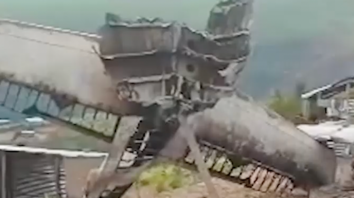 Wreckage of a crashed aircraft lies scattered beside a damaged structure and debris.
