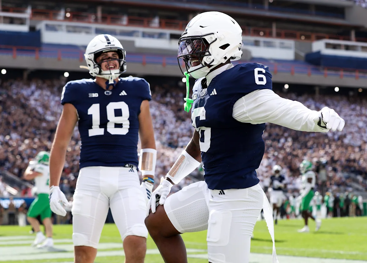 Penn State football players in navy uniforms celebrate during a game in a crowded stadium.
