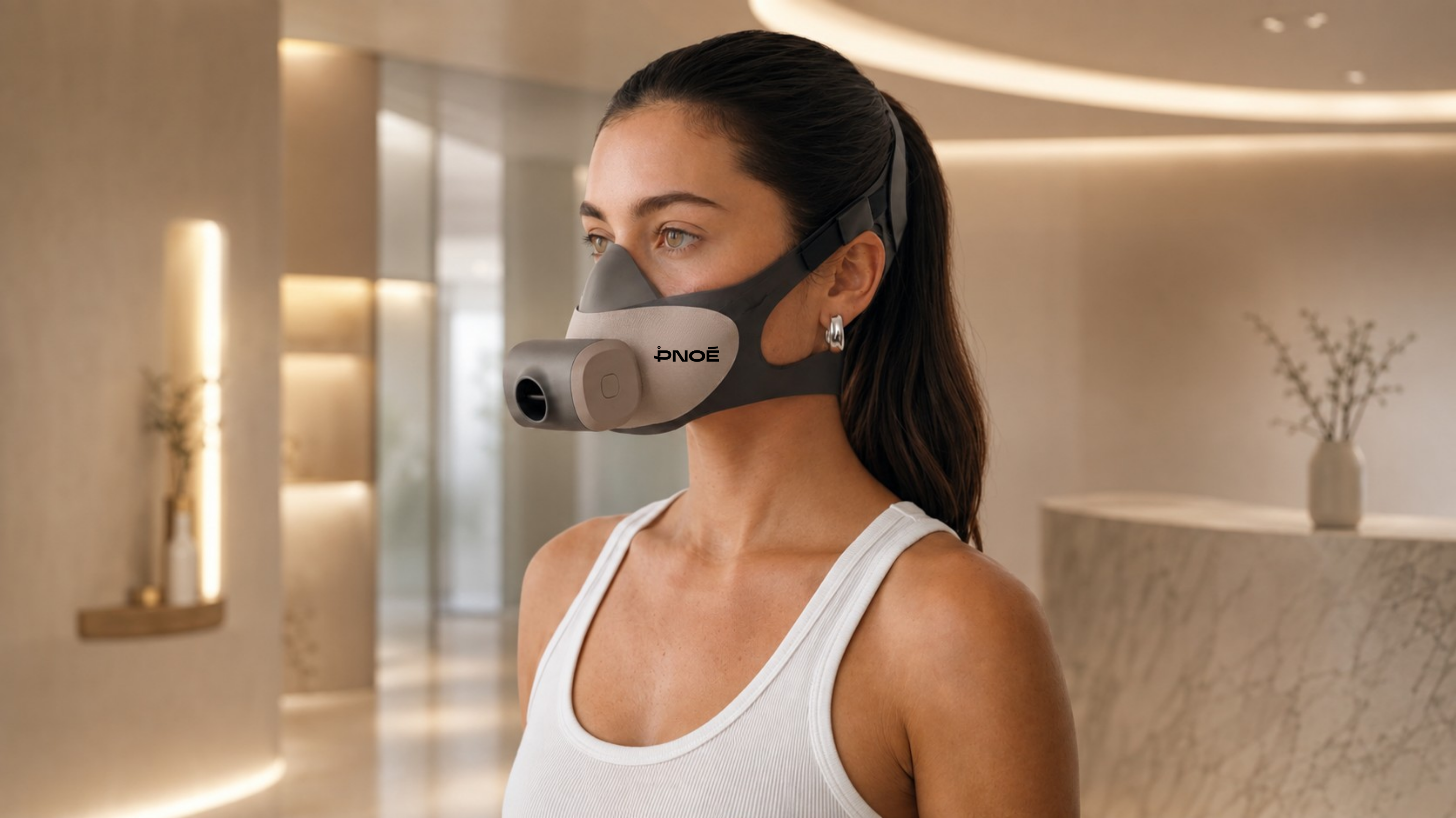 Woman wearing a gray PNOE-branded breathing mask in a softly lit interior.