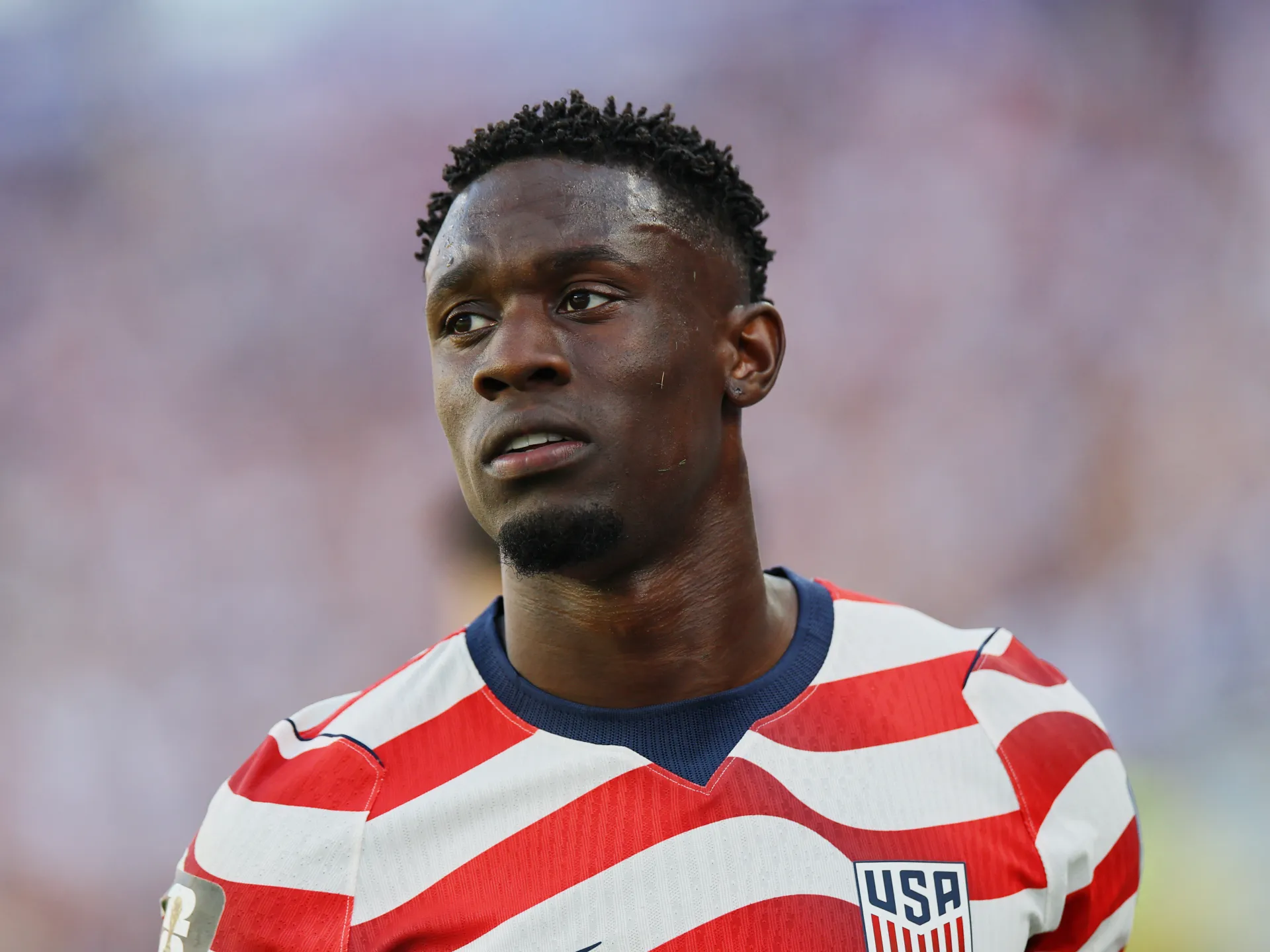 Close-up of a soccer player in a red-and-white striped USA jersey looking to the side.