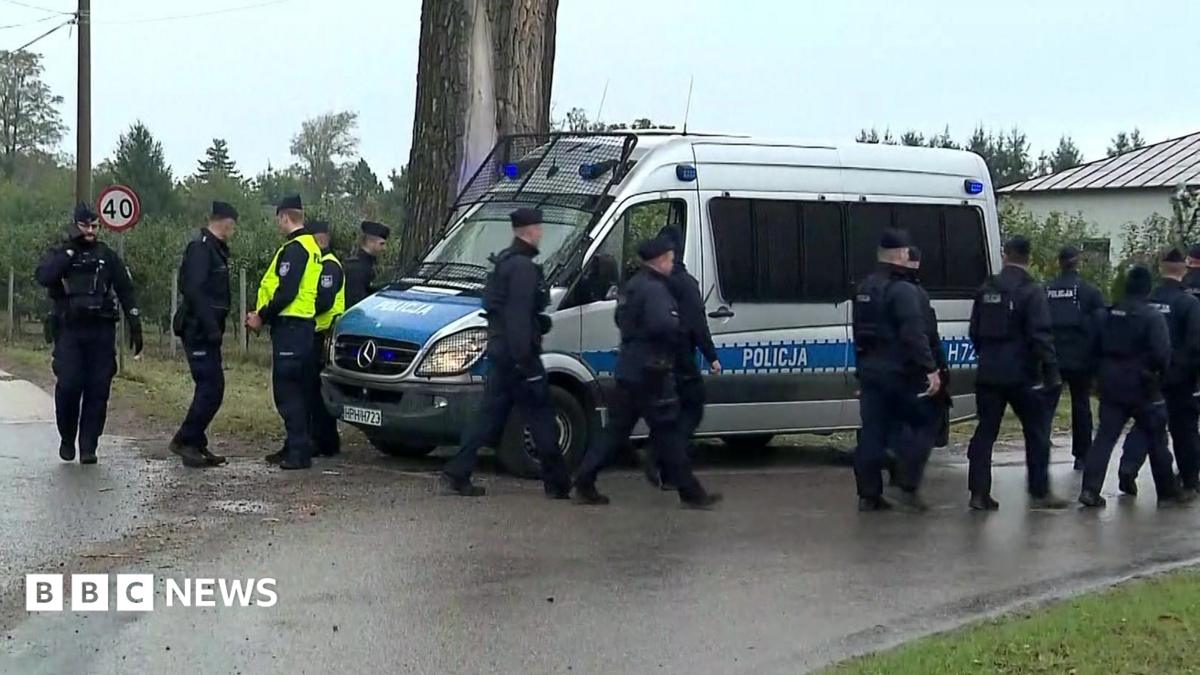 Uniformed officers stand beside a marked police van on a road near a building.