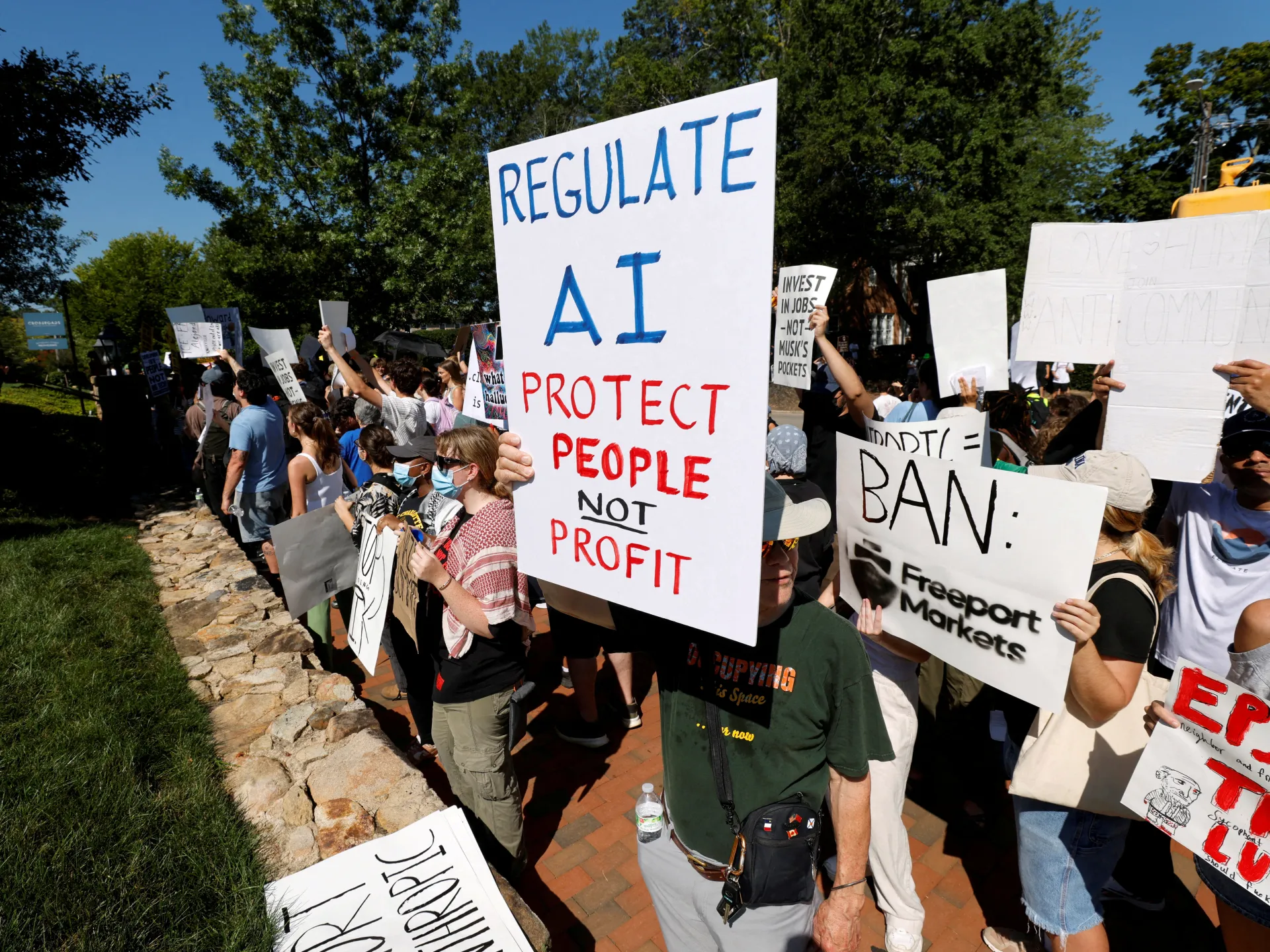 Crowd holds signs calling for AI regulation and protection of people during an outdoor protest.