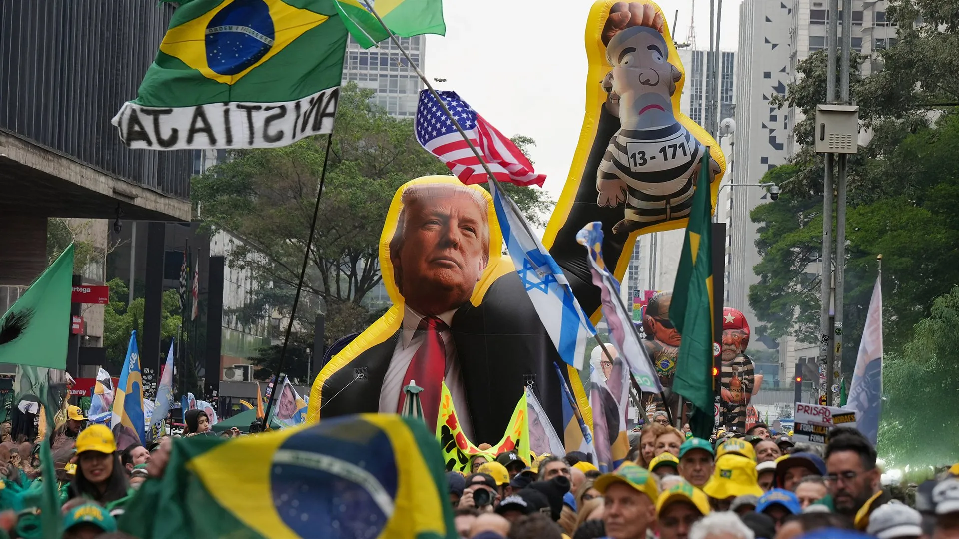 Crowd waving Brazilian flags beside inflatable figures of Donald Trump and a prisoner