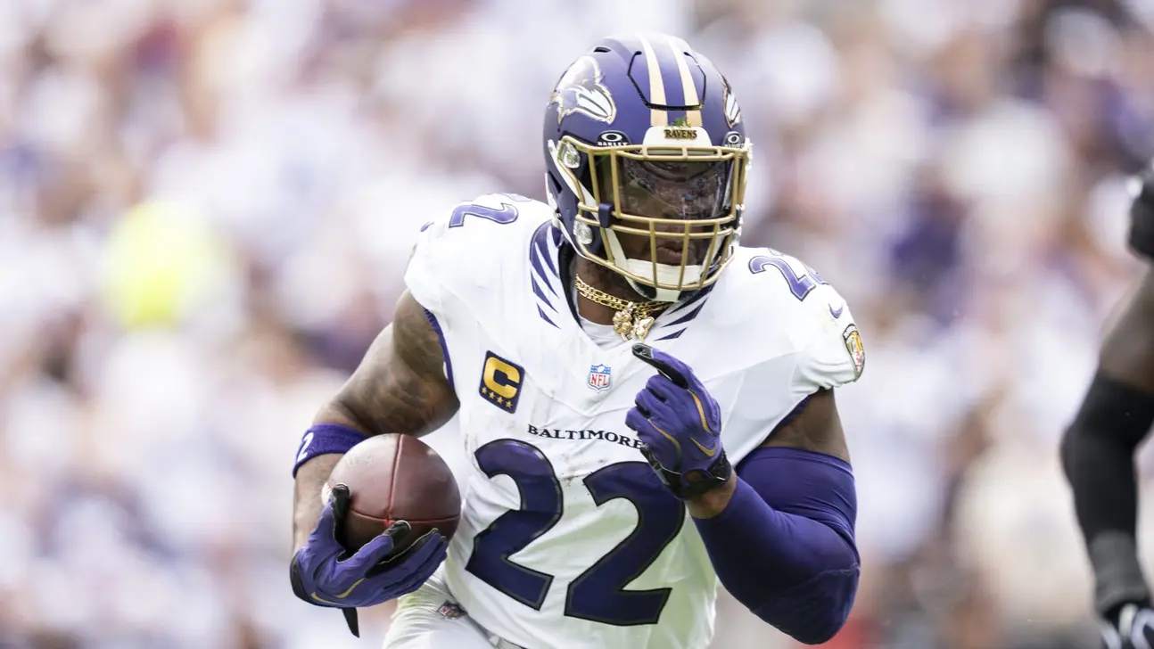 A Baltimore Ravens player in a white number 22 uniform runs with a football during a game.
