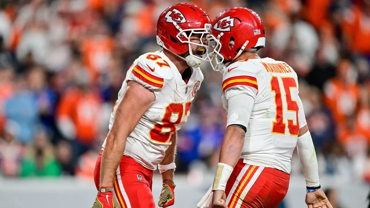 Two Kansas City Chiefs players in red helmets and white uniforms celebrate on the field