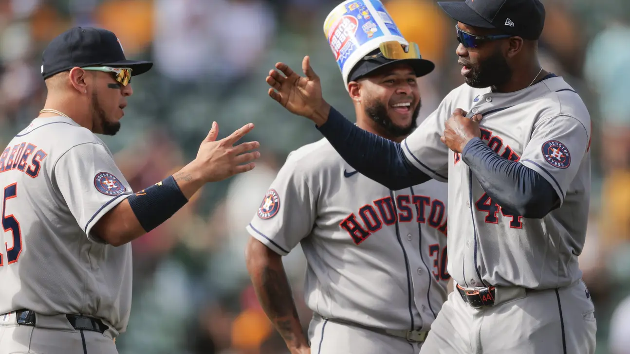 Three Houston Astros players celebrate together, one wearing an oversized promotional bucket on his head.