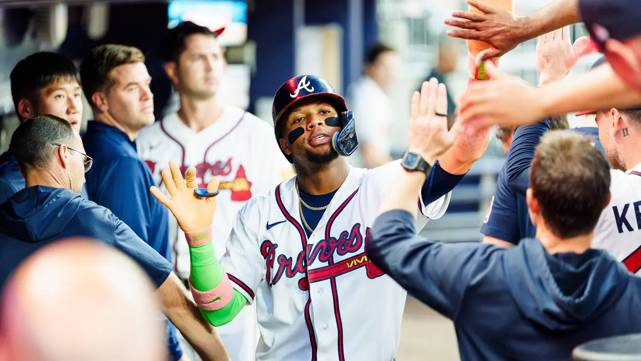 Atlanta Braves player high-fives teammates in the dugout while wearing a batting helmet and white jersey.
