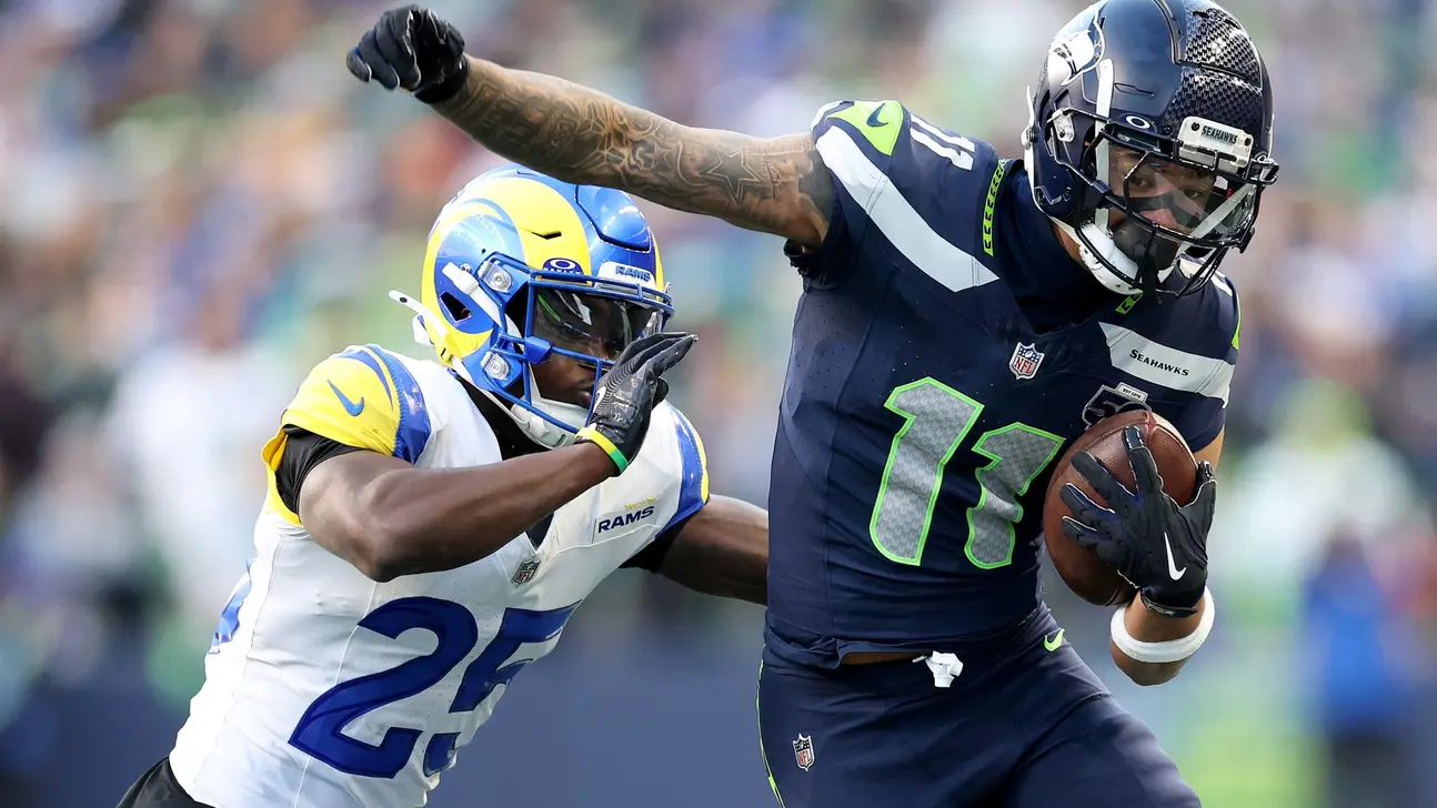 Seattle Seahawks player runs with the football as a Los Angeles Rams defender reaches toward him.