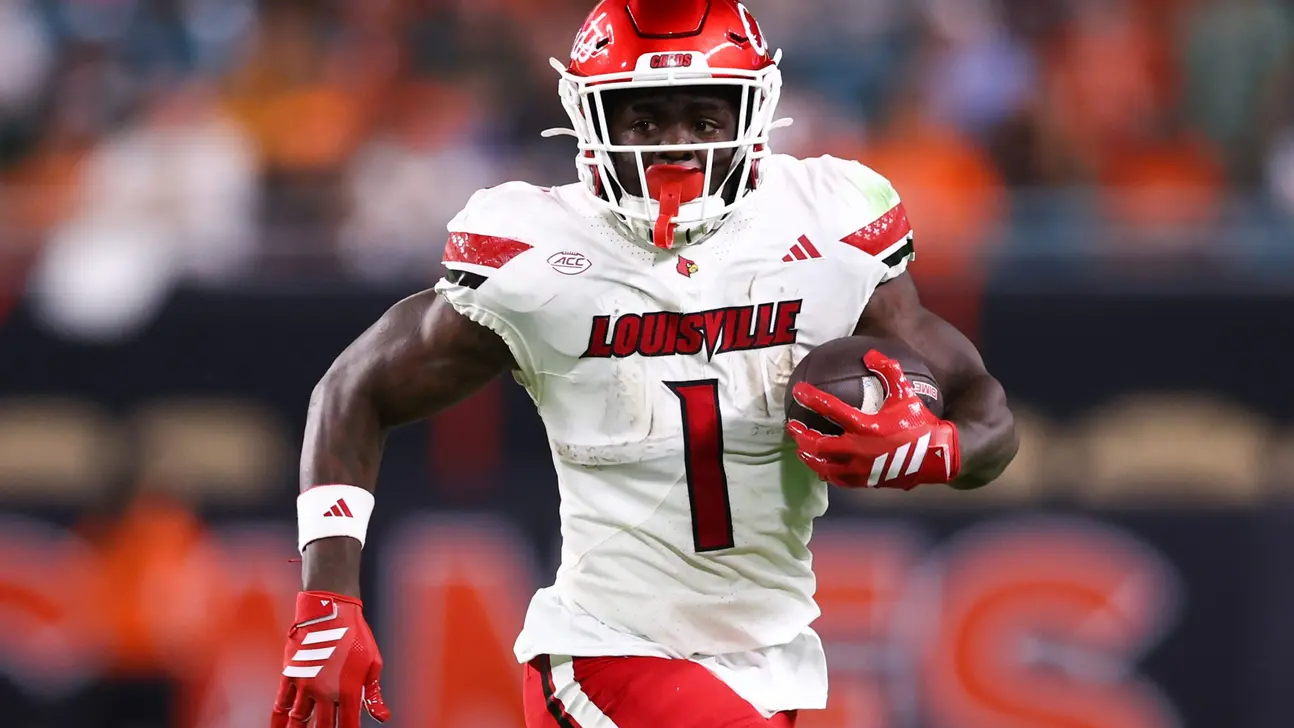 Louisville football player in white uniform runs with a football during a game
