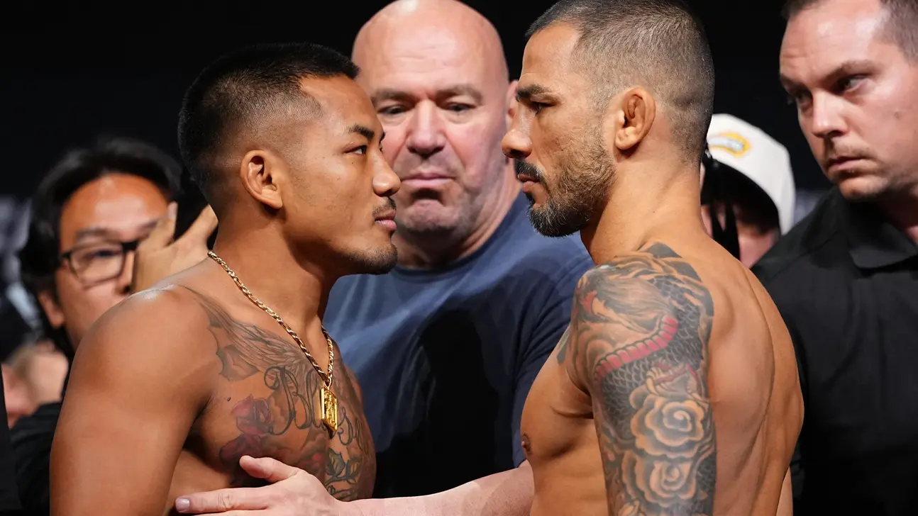 Two tattooed fighters face off during a tense weigh-in while officials and spectators watch behind them.