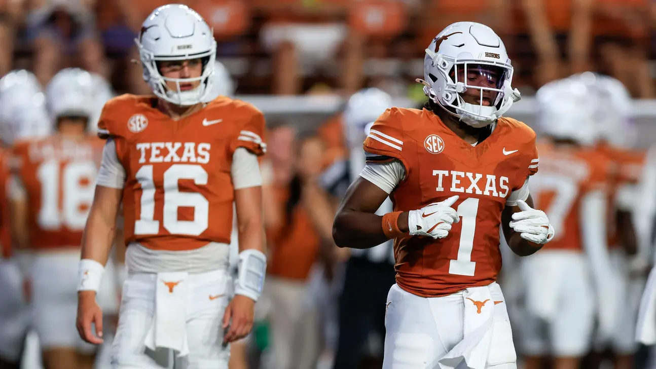 Two Texas football players in orange jerseys and white helmets on the field