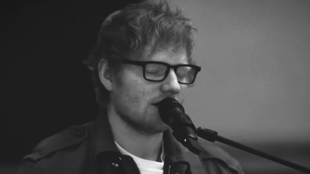 Black-and-white close-up of a bespectacled musician singing into a microphone.