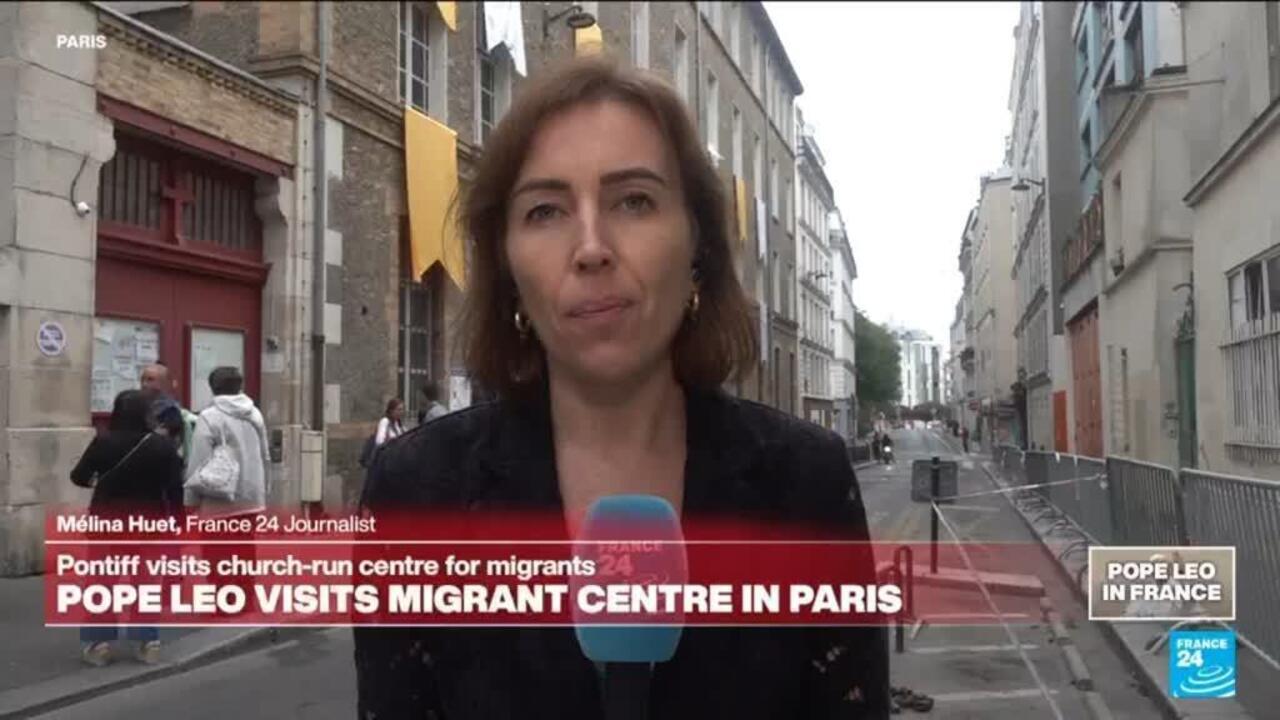 A female reporter stands on a Paris street holding a microphone, with a news banner about a migrant centre visit.