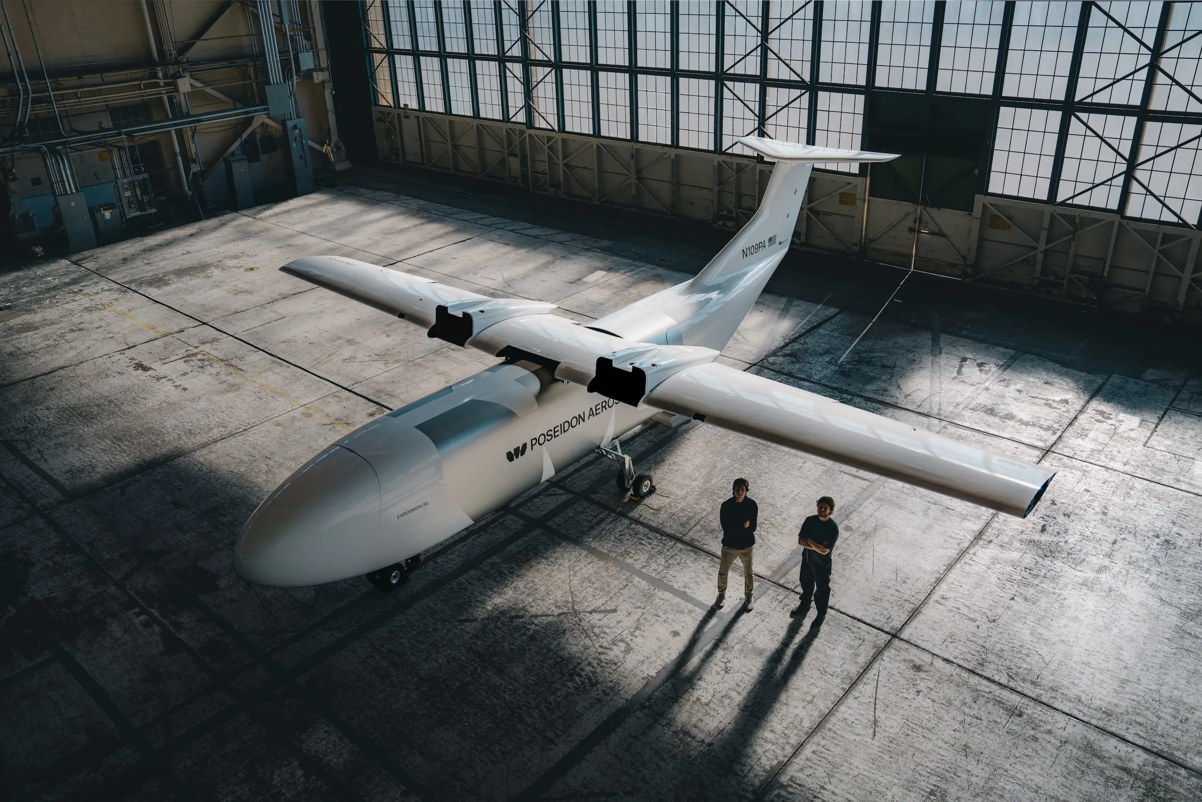 White Poseidon Aerospace aircraft parked inside a hangar beside two people.