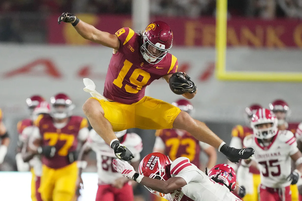 USC football player leaps over defenders while carrying the ball during a game.
