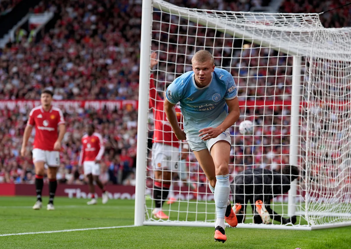 Manchester City player in blue runs from the goal as Manchester United players stand behind him