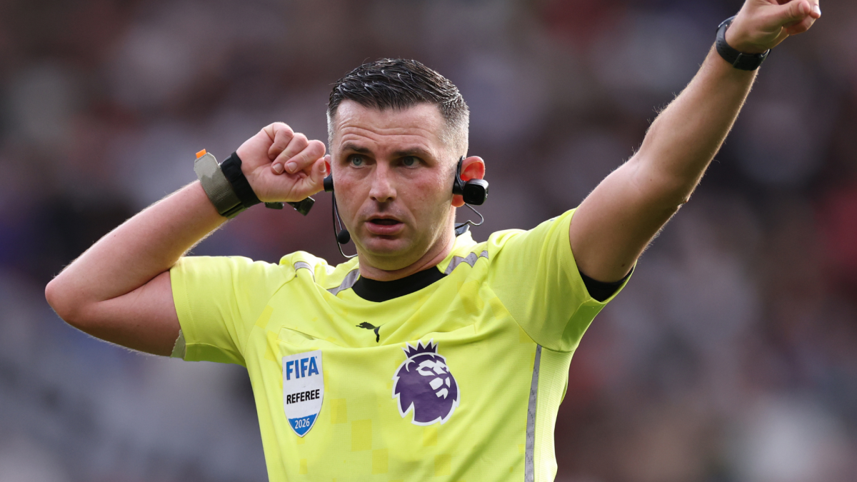 Football referee in a fluorescent yellow shirt signals with one arm raised during a match.