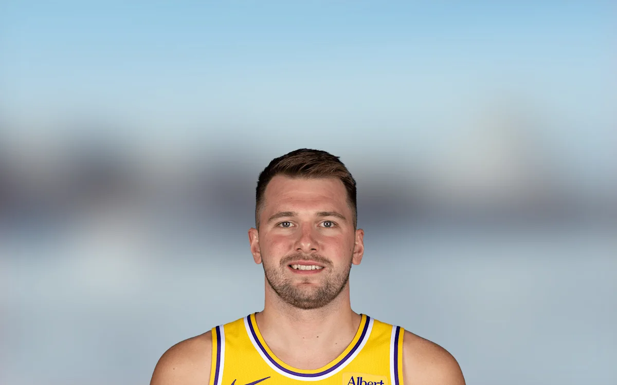 Basketball player in a yellow and purple jersey smiles against a blurred blue-gray background.