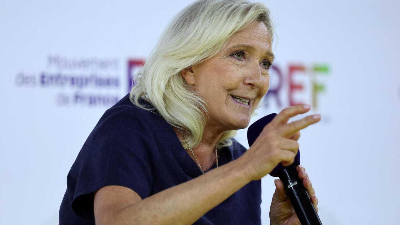 Blonde woman speaking into a microphone and gesturing during a public event