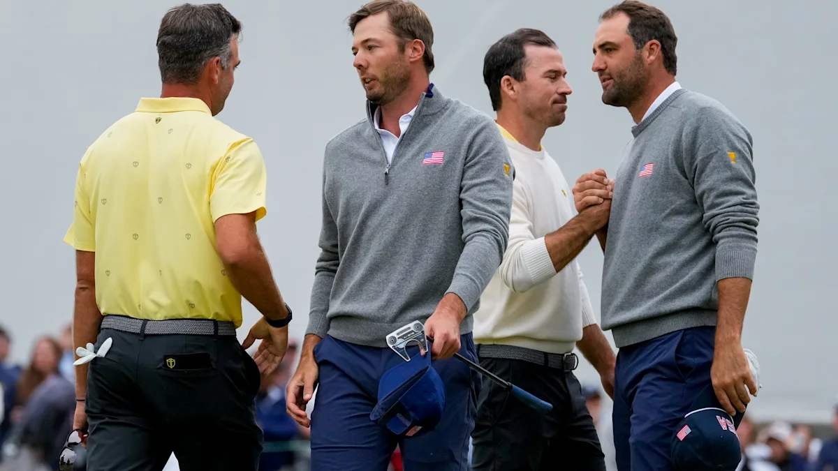 Two golfers in gray sweaters stand near a golfer in a yellow shirt on a course.