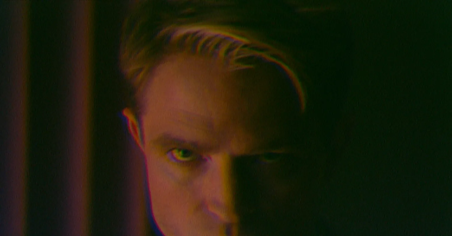 A close-up of a person with short hair looking sideways against a dark background.