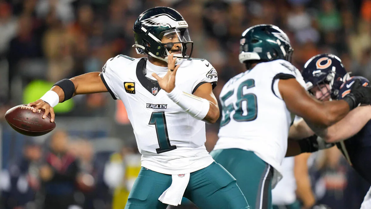 Philadelphia quarterback in a white number 1 jersey prepares to throw as teammates block defenders.