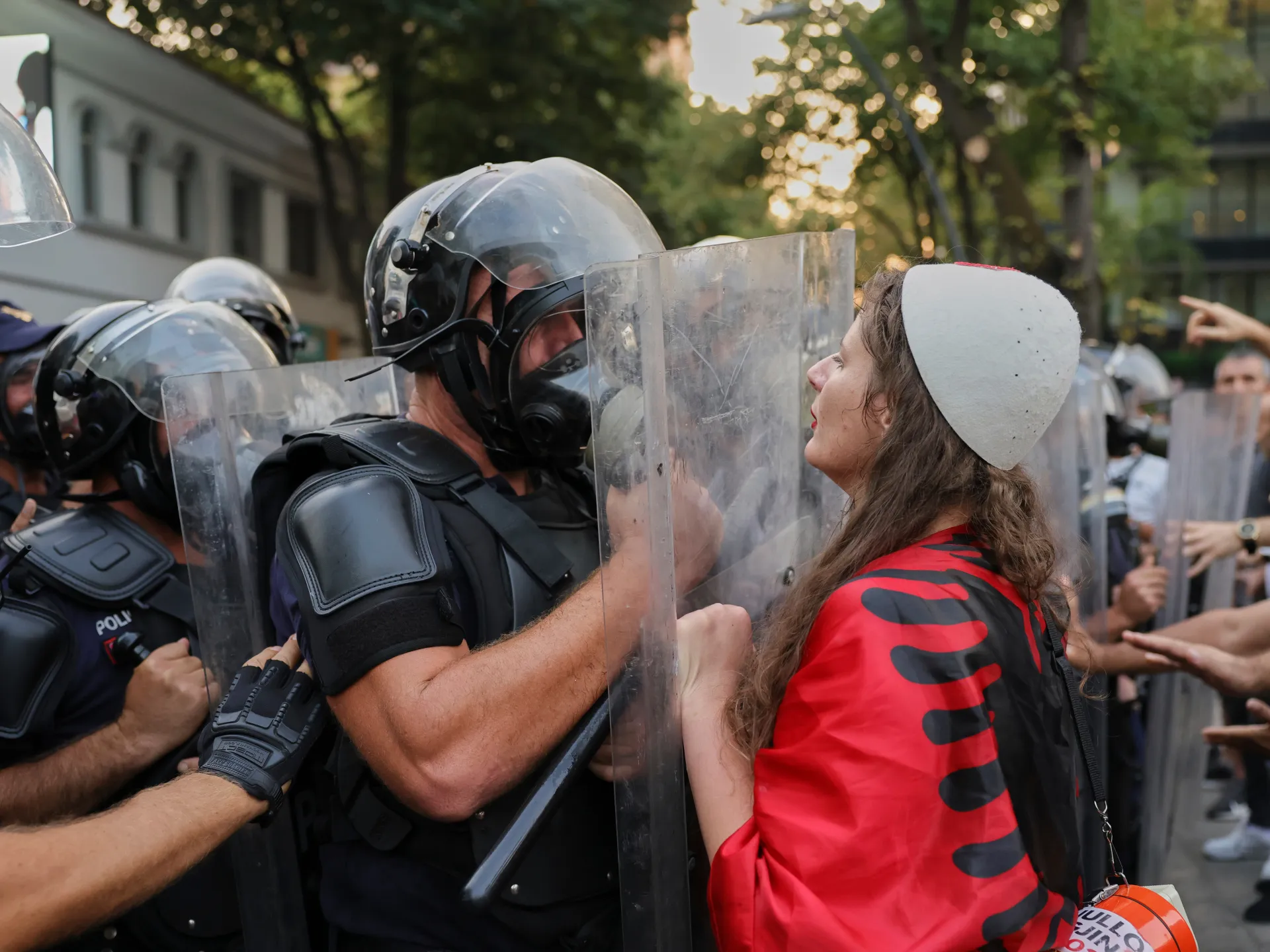 Protester in red shirt faces riot police holding clear shields during a tense street confrontation