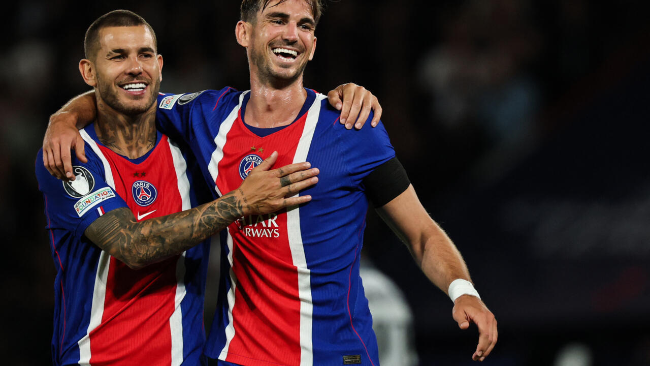 Two Paris Saint-Germain players smile and embrace while wearing matching blue, red and white jerseys.