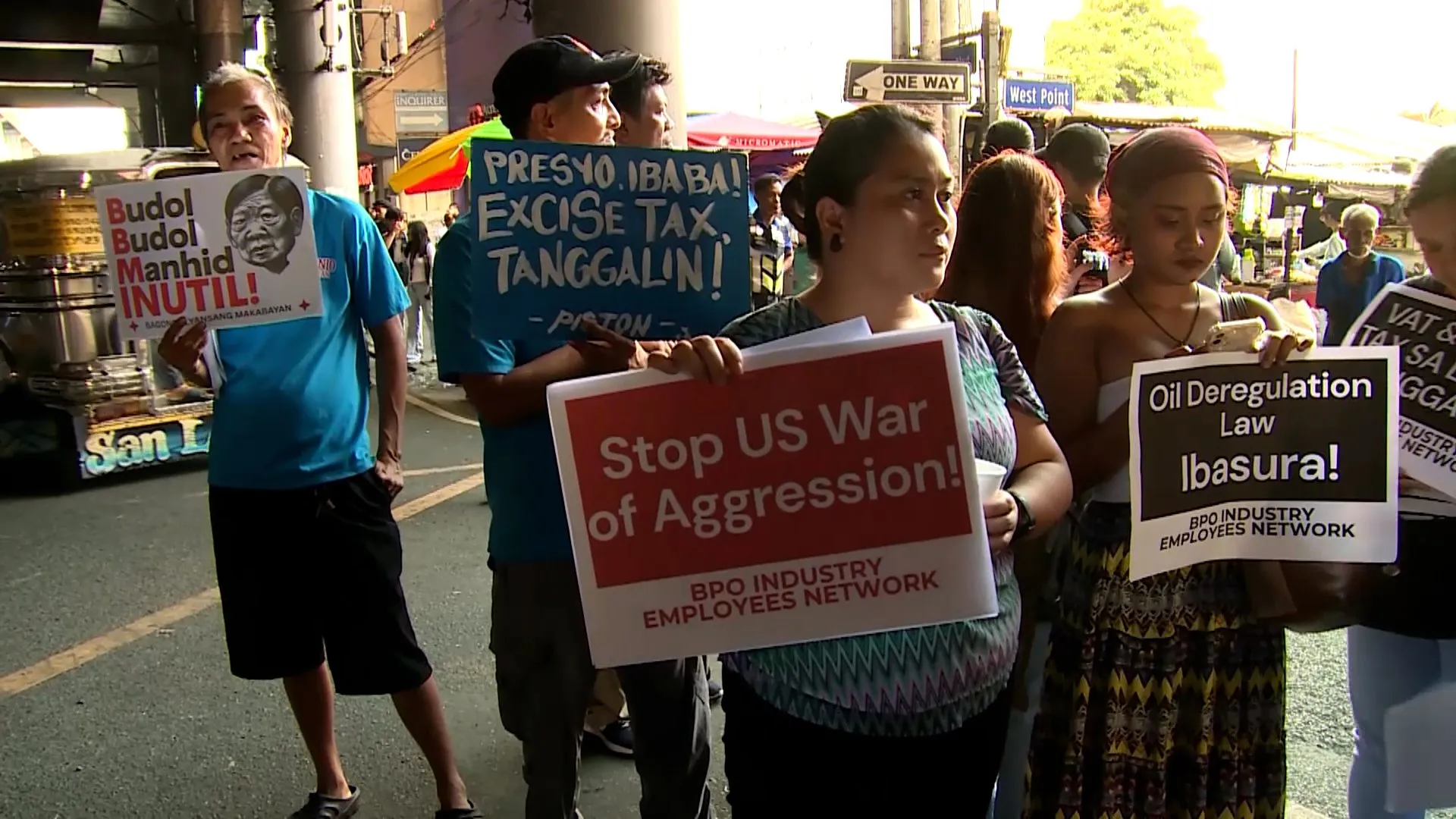 People hold protest signs on a busy street, including messages about fuel taxes, oil deregulation, and war.
