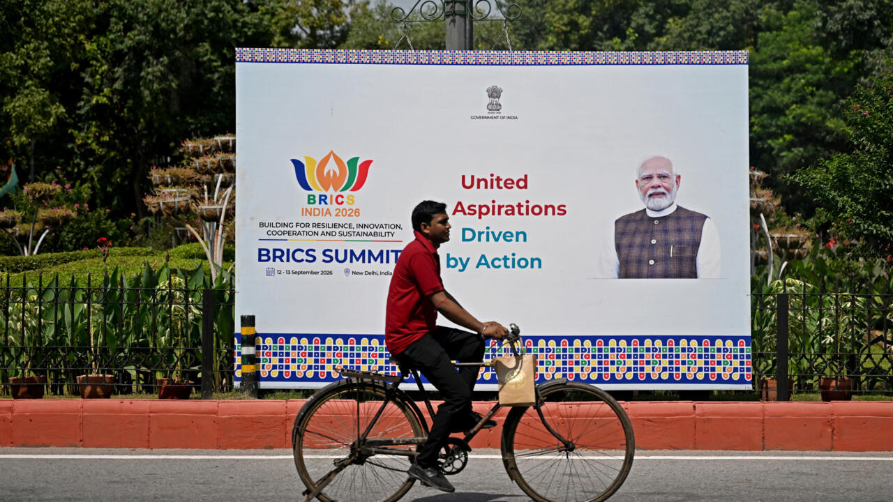 A cyclist rides past a BRICS India 2026 summit billboard featuring Narendra Modi.