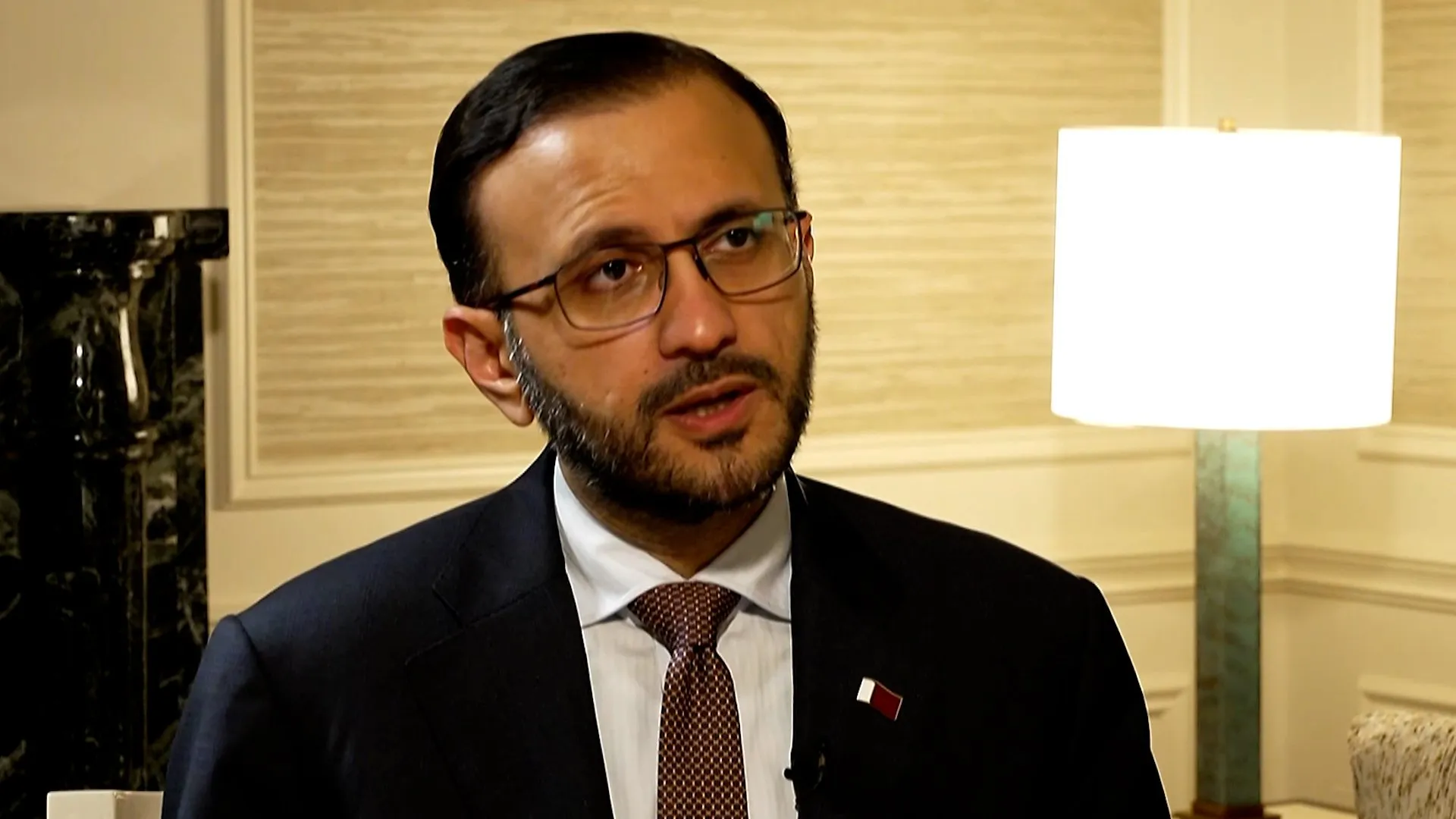 A man in glasses and a dark suit speaks on camera, with a blank white rectangle at right.