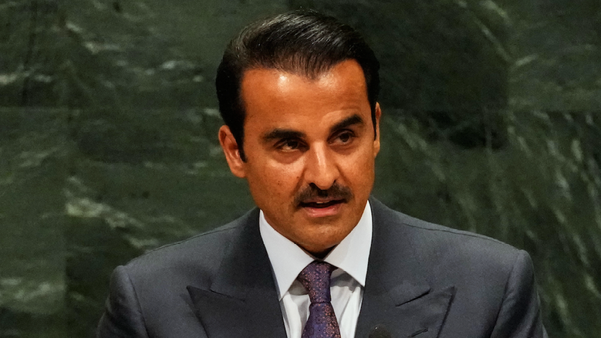 Man in a dark suit and patterned tie speaks against a dark green marble backdrop.