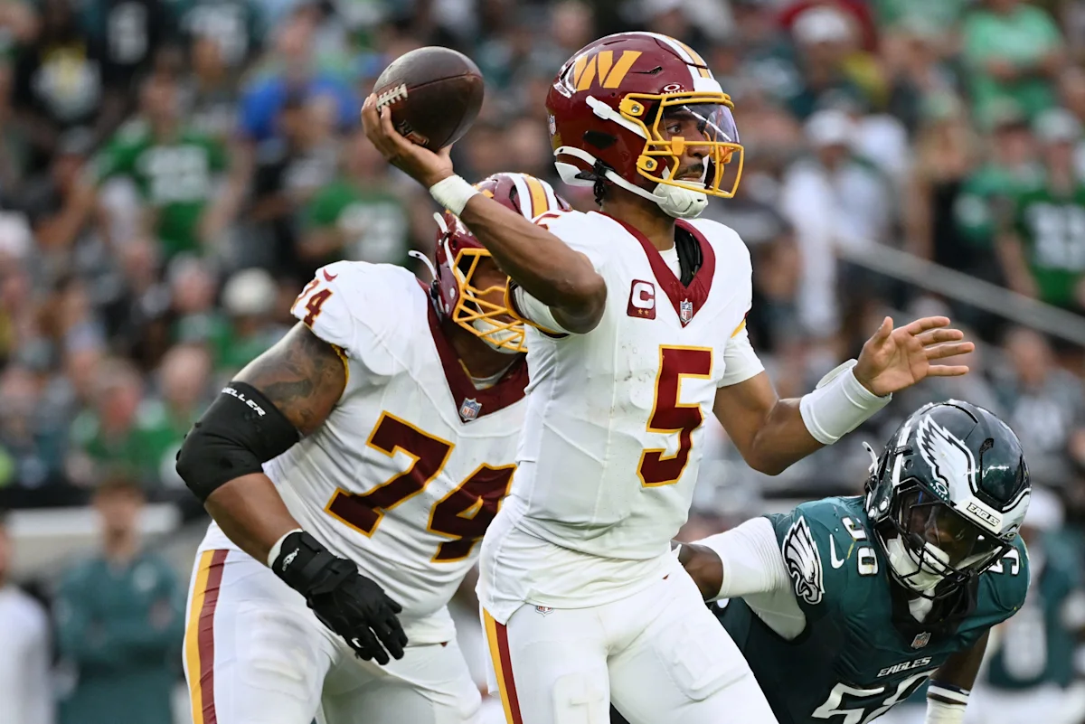 Washington quarterback throws a football as teammates block an Eagles defender during an NFL game.