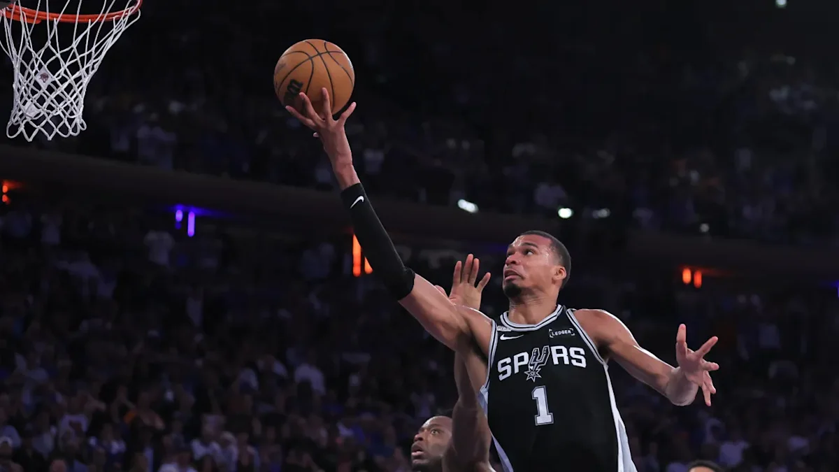 Basketball player in a Spurs number 1 jersey reaches toward the hoop for a layup.