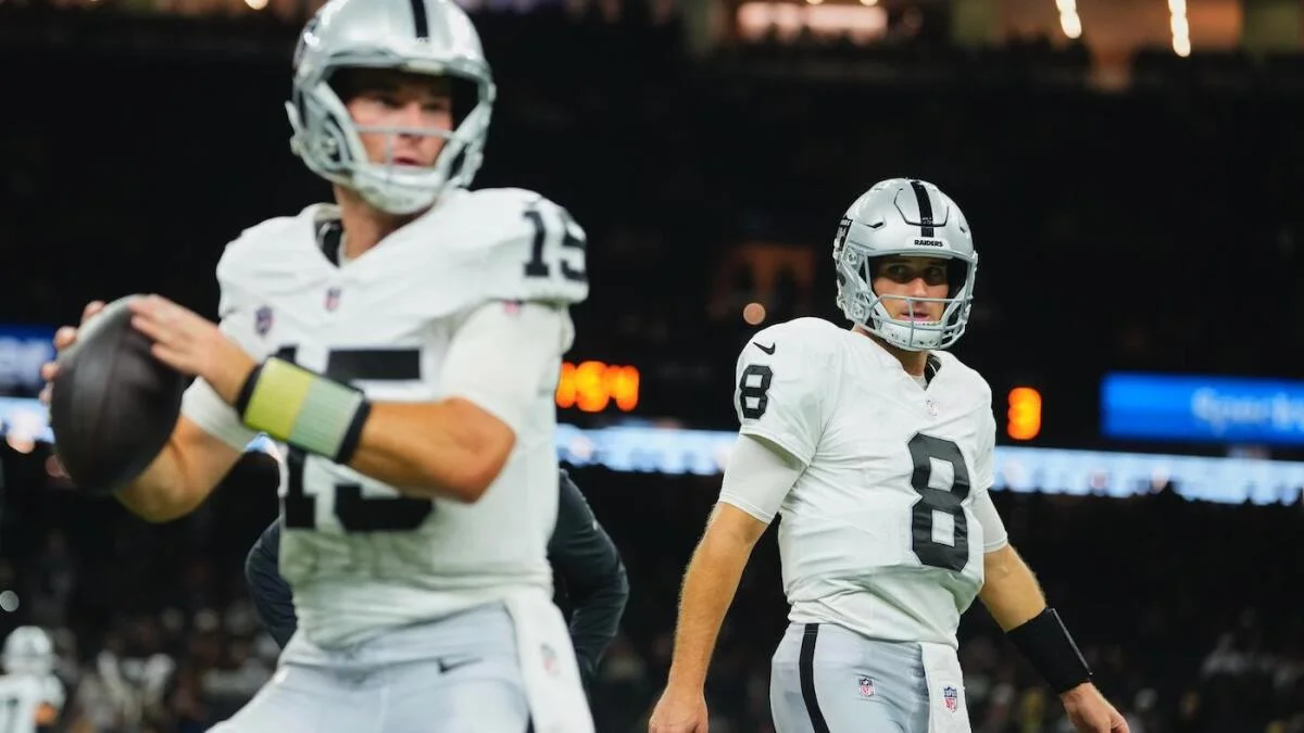 Two Raiders players in white uniforms, one holding a football in the foreground and another standing behind him.