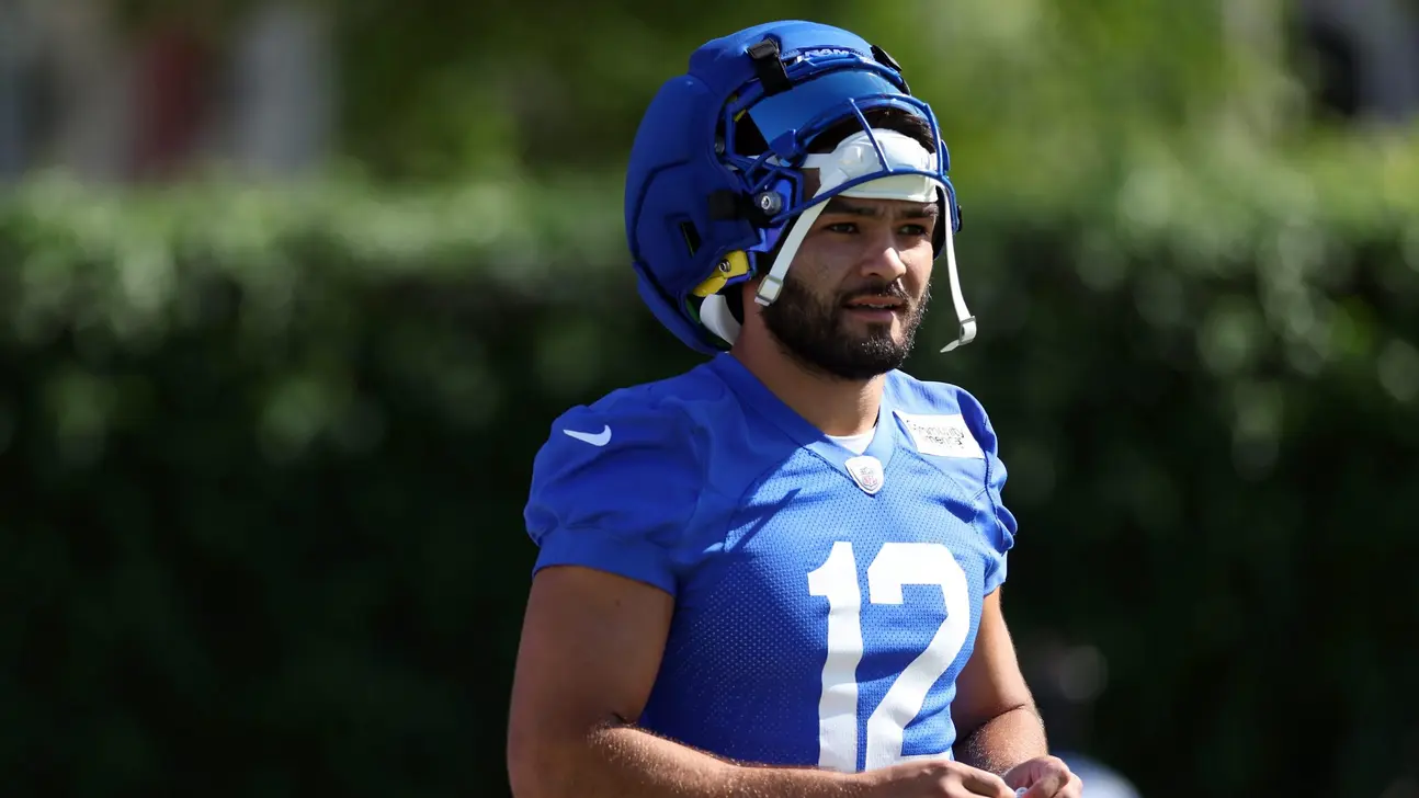 Football player in blue uniform and helmet stands outdoors during practice
