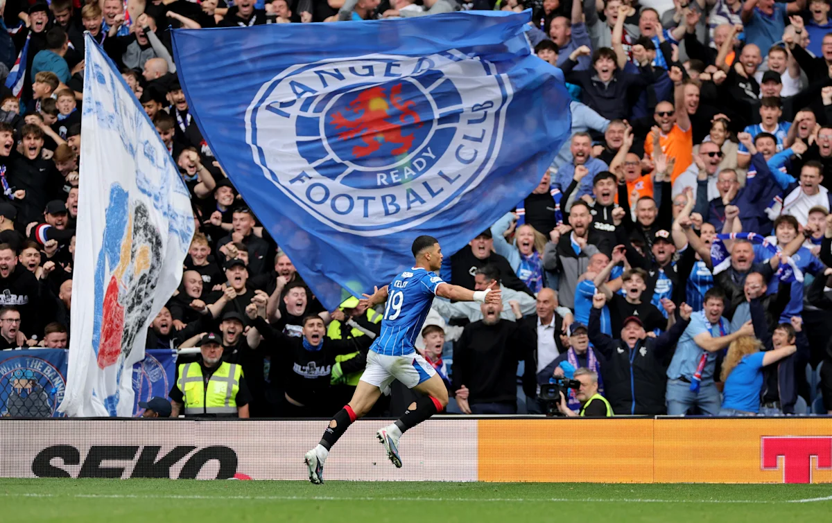 Rangers player celebrates before jubilant supporters waving large blue club flags