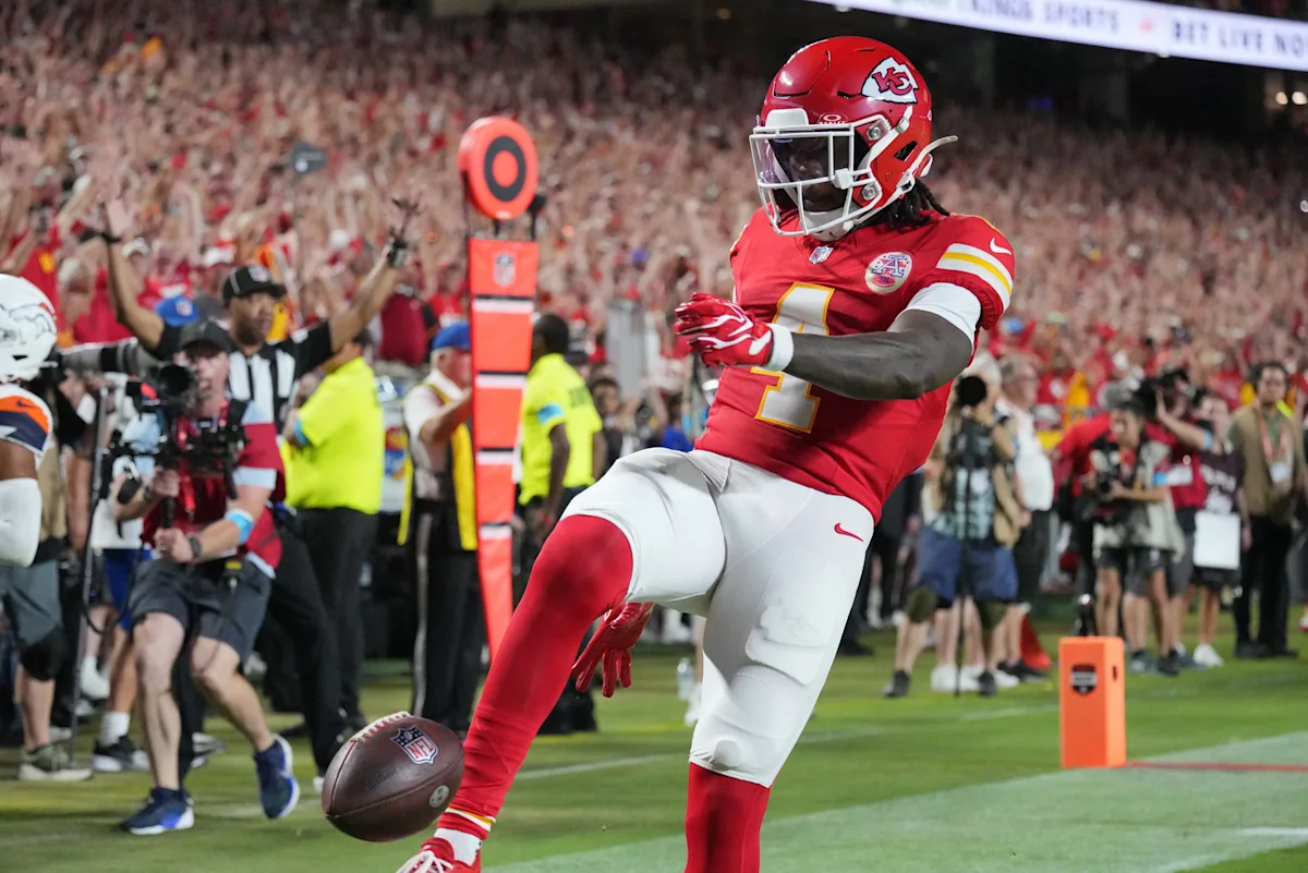 Football player in red uniform celebrates near the end zone as a football bounces nearby.