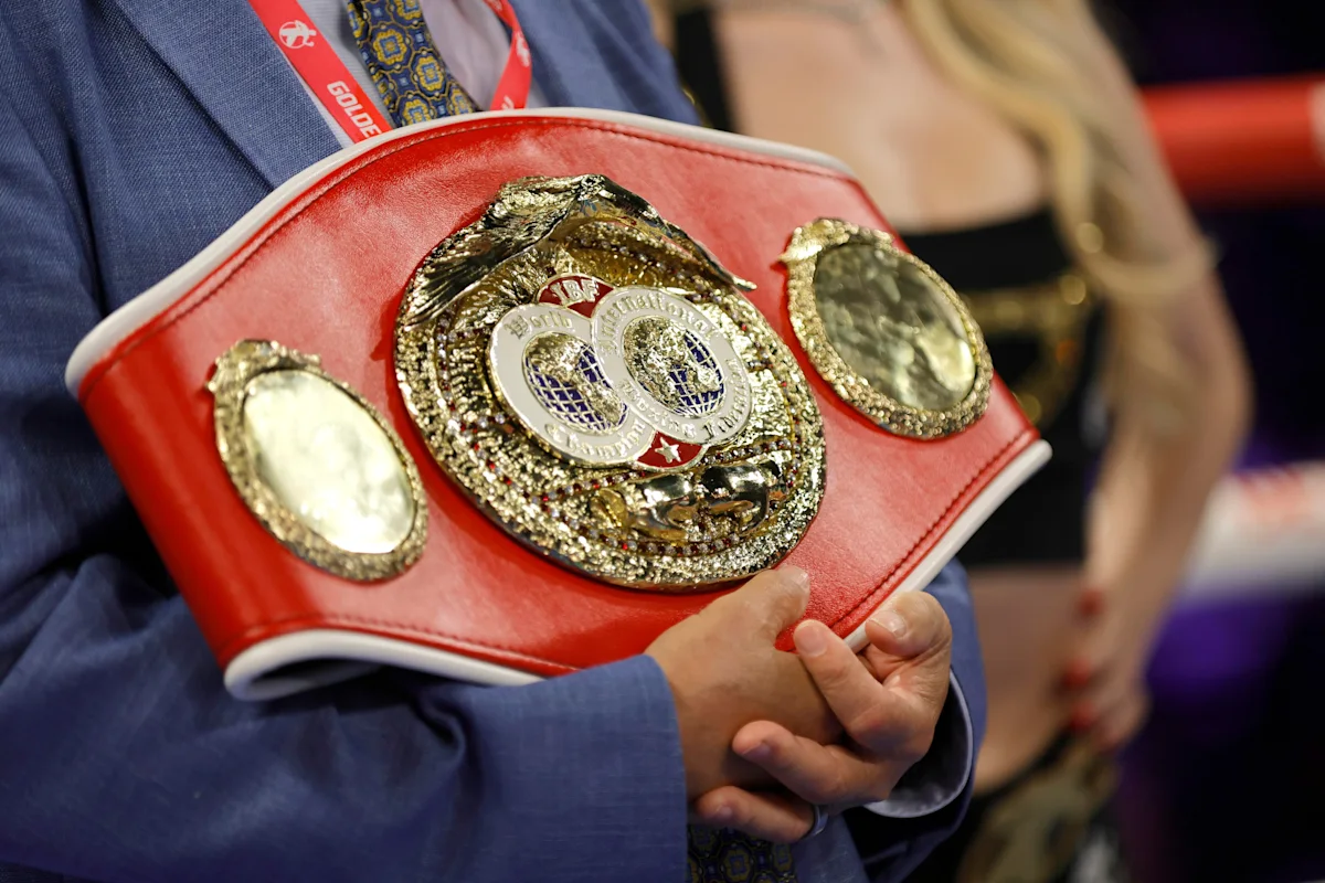 Red-and-gold championship boxing belt held by a person wearing a blue suit
