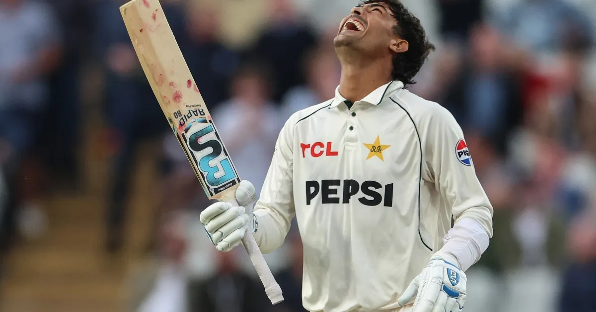 Cricketer in white Pakistan Test uniform celebrates while holding a raised bat.