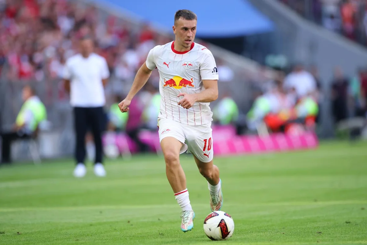 Footballer in a white RB Leipzig kit runs with the ball during a match.