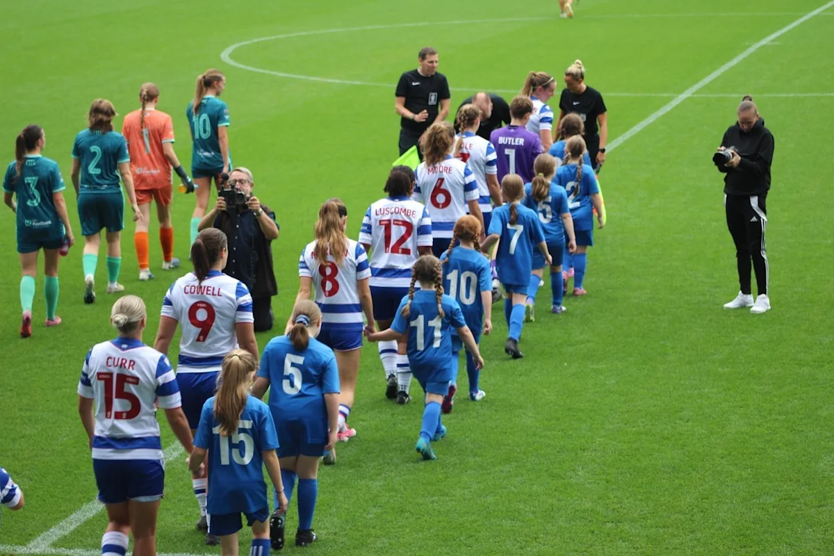 Women’s football players and young mascots walk across the pitch after a match.