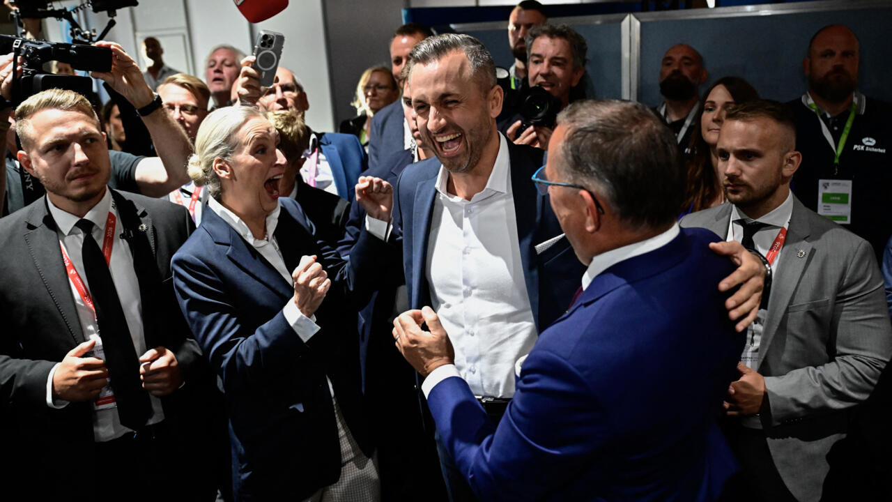 Politicians and supporters celebrate amid journalists and photographers at a crowded indoor event.