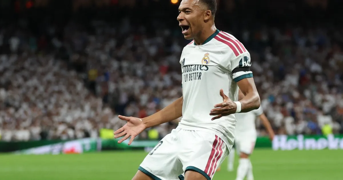 Real Madrid forward in white kit celebrates with arms outstretched during a match