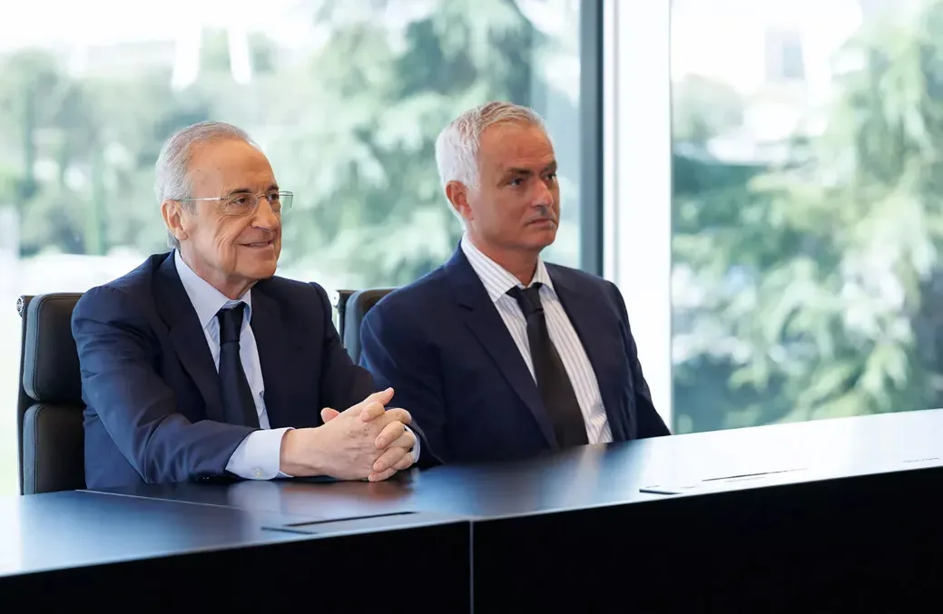 Two suited men sit together at a conference table in a bright office.