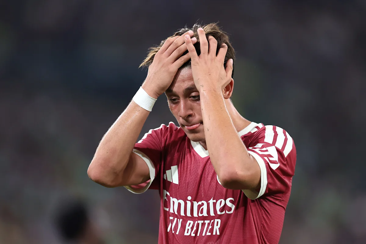 Footballer in red jersey holding his head, appearing distressed during a match.