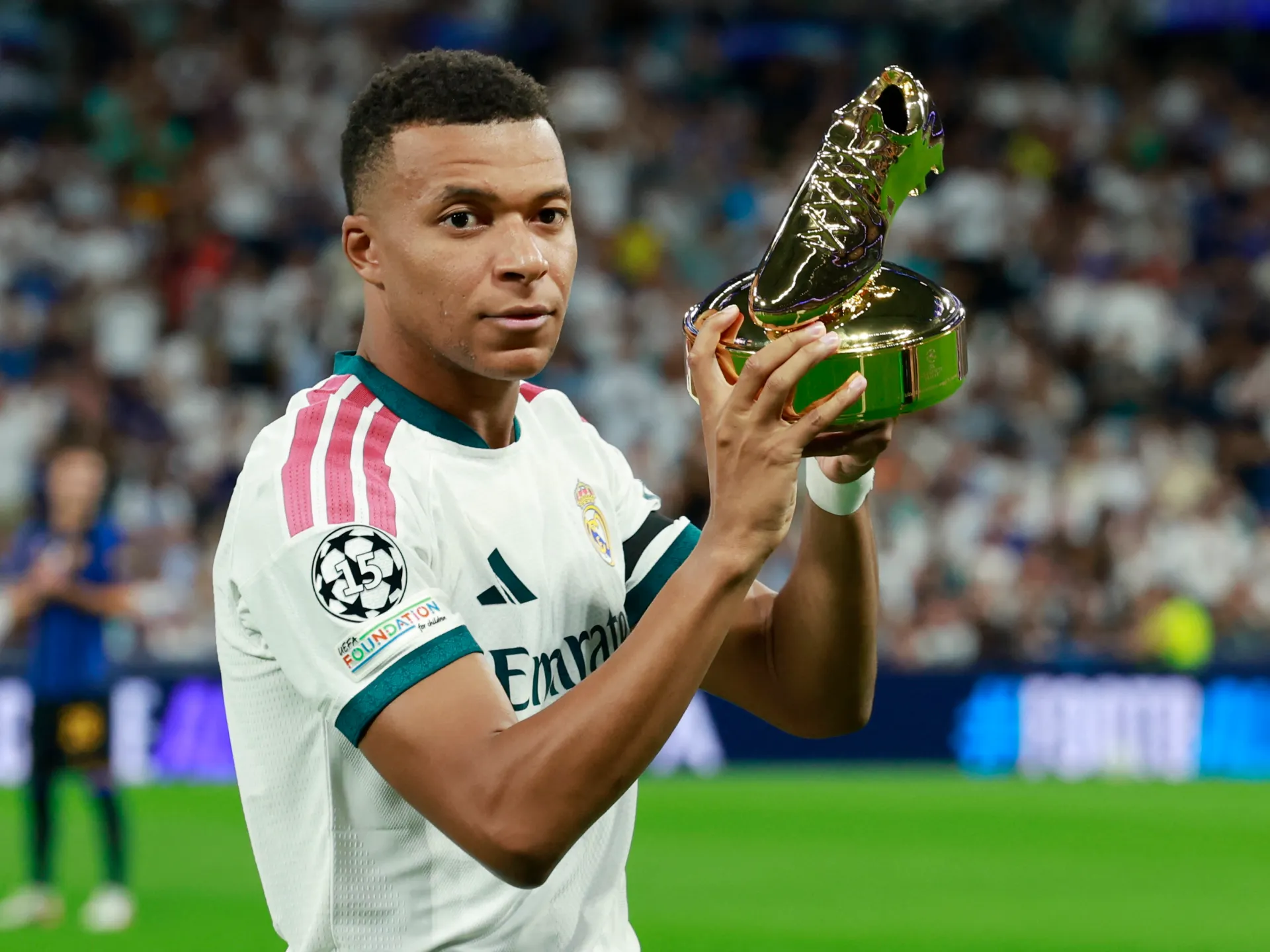 Footballer in a Real Madrid jersey holds a golden boot-shaped trophy during a stadium celebration.
