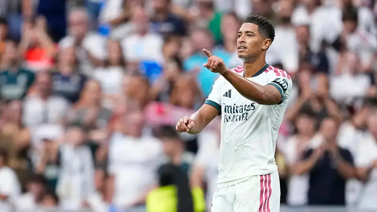 A footballer in a white Real Madrid kit points toward the stands during a match.