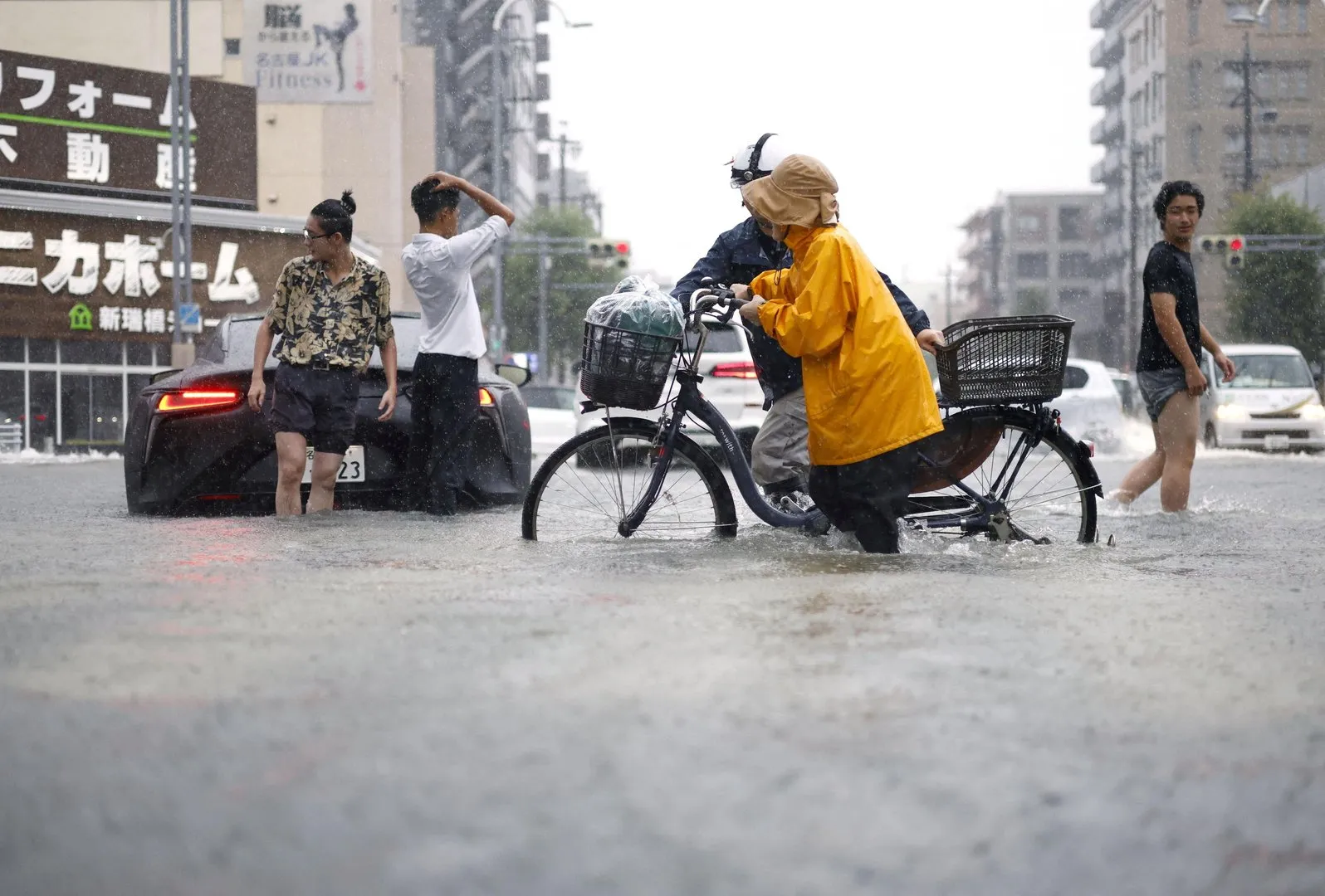People wade through deep floodwater as a cyclist pushes a bicycle during heavy rain.