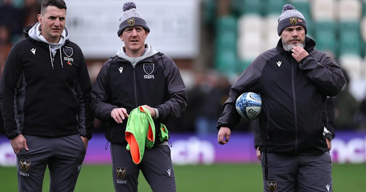 Three rugby coaches in Saints training gear stand on the touchline, one holding a ball and another training bibs.